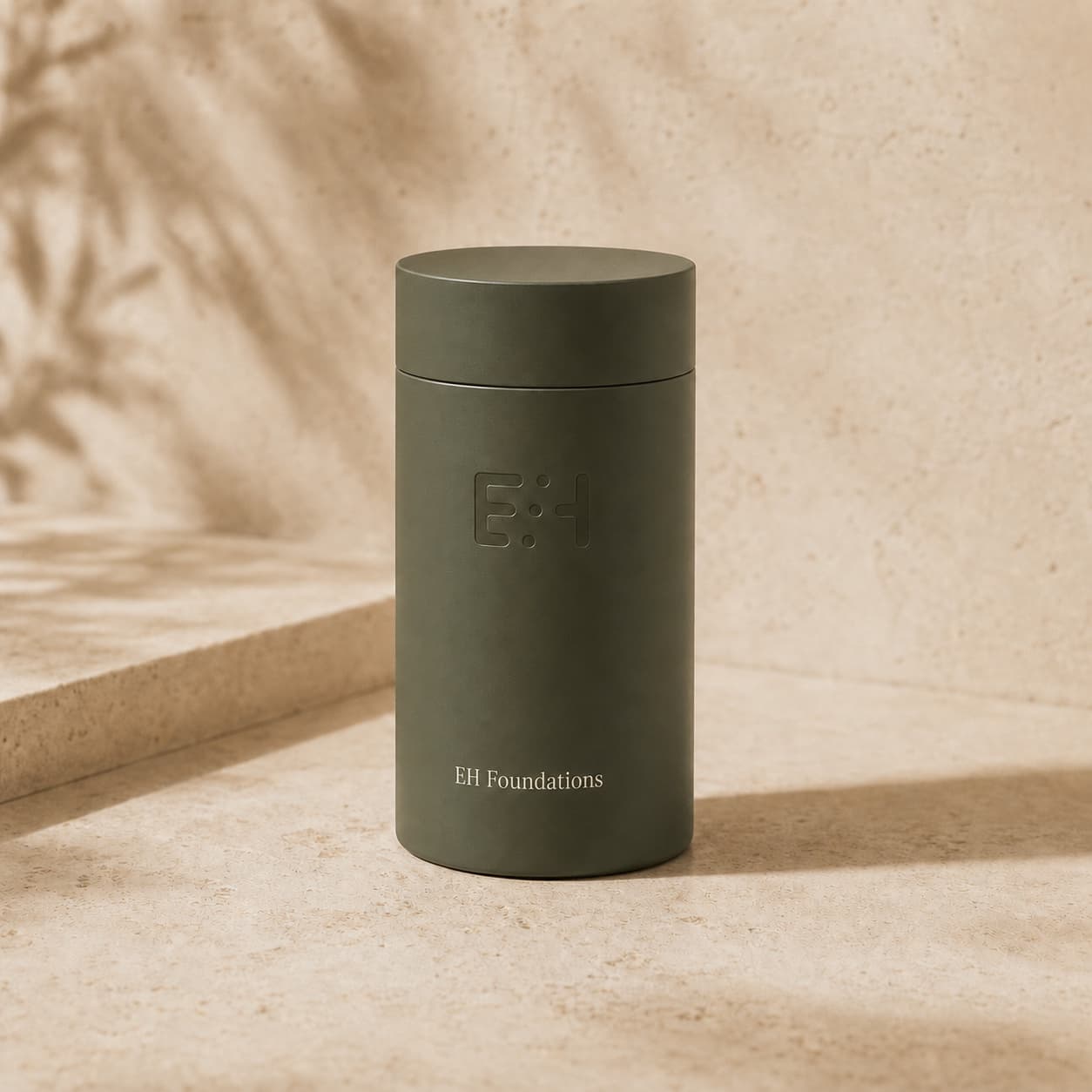 Tall deep-sage EH Foundations bottle on warm travertine